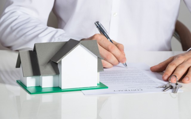 Midsection of businessman signing house contract at office desk